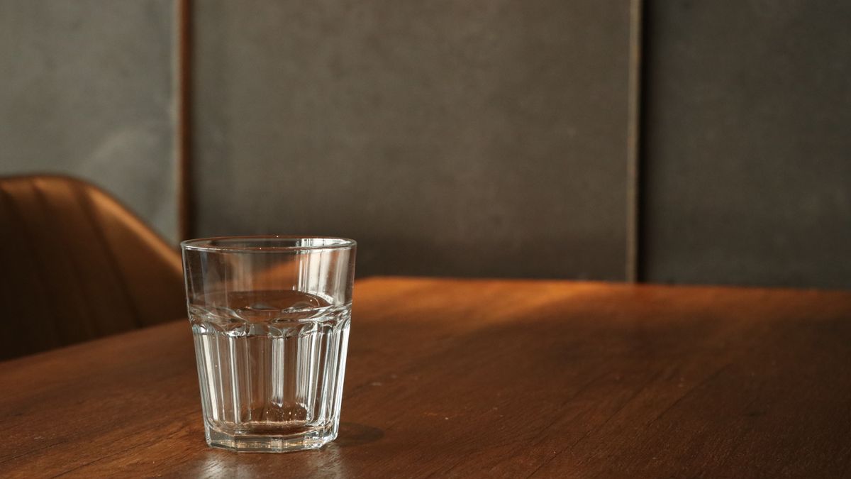 A single glass of water on a sunlit wooden table