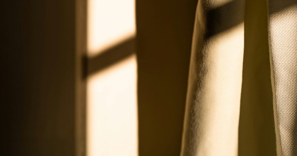 Late afternoon light falling through a window and across a pale curtain and wall