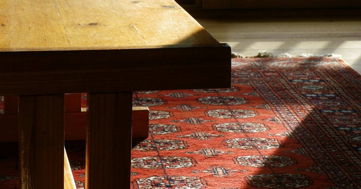 Afternoon sunlight falling across a patterned red rug beside the corner of a wooden table