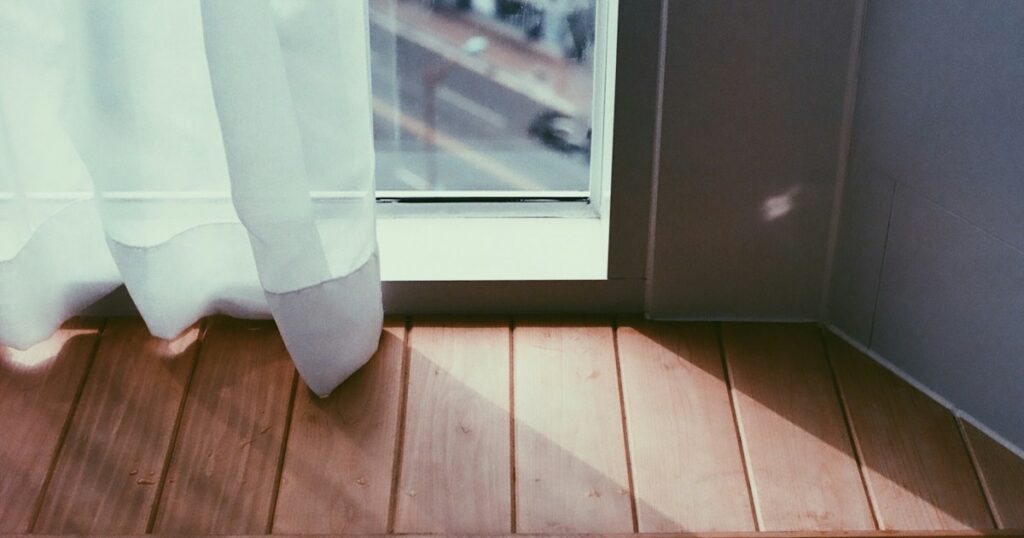 Late afternoon sunlight falling across a wooden floor beside a window with a pale curtain