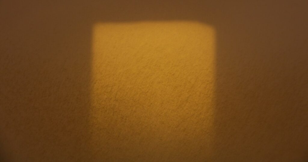 A square of afternoon window light falling on a bare textured wall