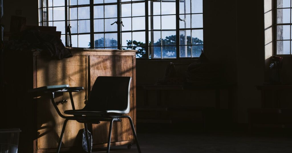 An empty armchair and a wooden cabinet beside tall windows in a calm, daylit room