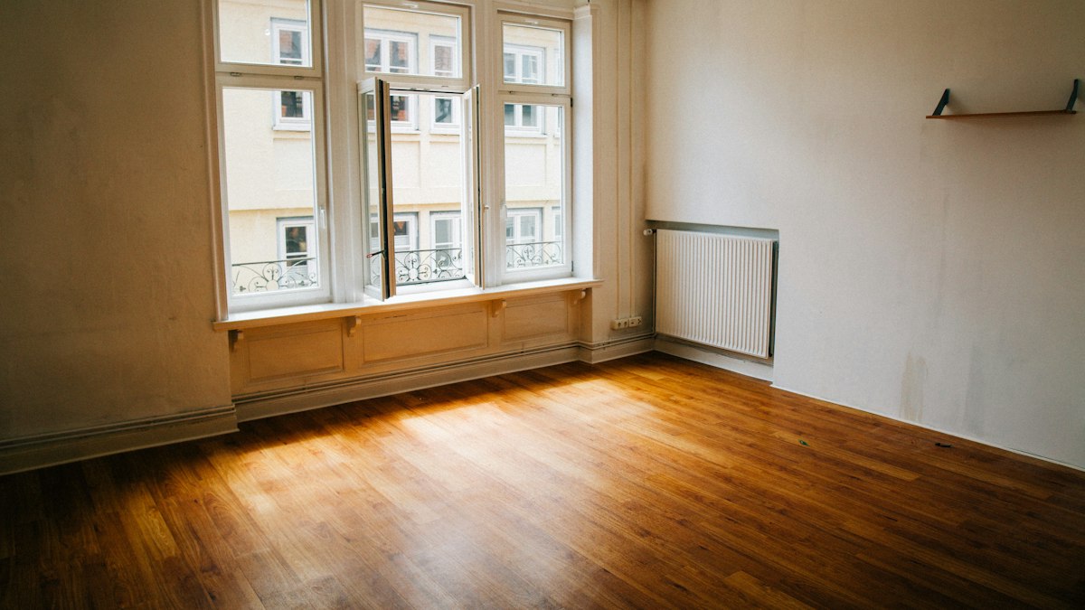 An empty flat with warm wooden floors and an open window