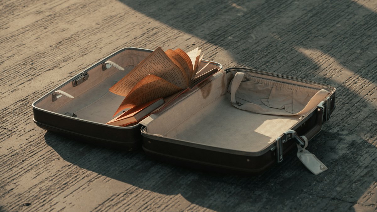 An open, almost empty suitcase with a book in it, on warm concrete