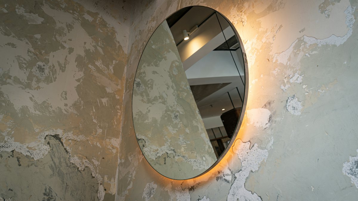 A backlit oval mirror on a bare plaster wall