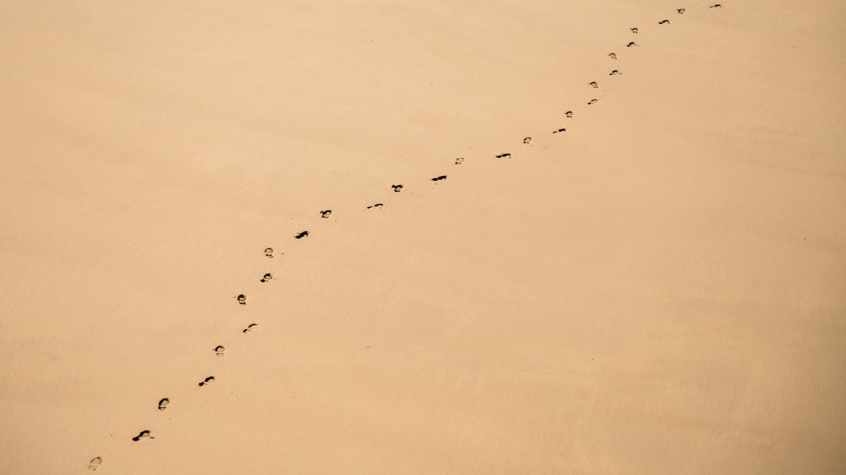 A line of footprints across smooth warm sand