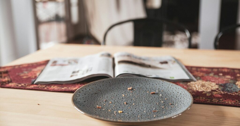 An empty plate with only crumbs left on it, on a wooden table in morning light