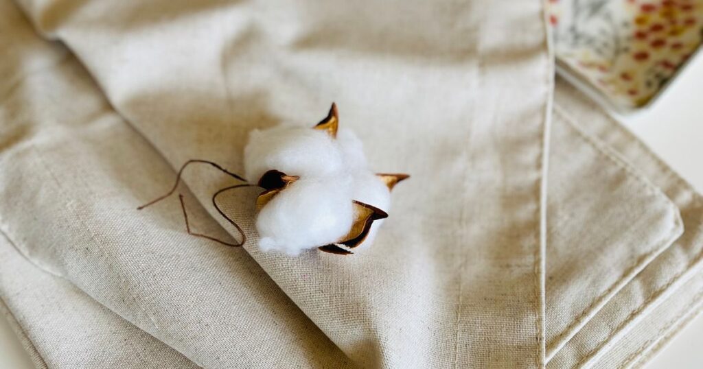 A cotton boll resting on folded beige linen in soft daylight