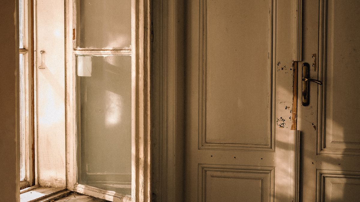 A warm cream door standing ajar beside an old window in late afternoon light