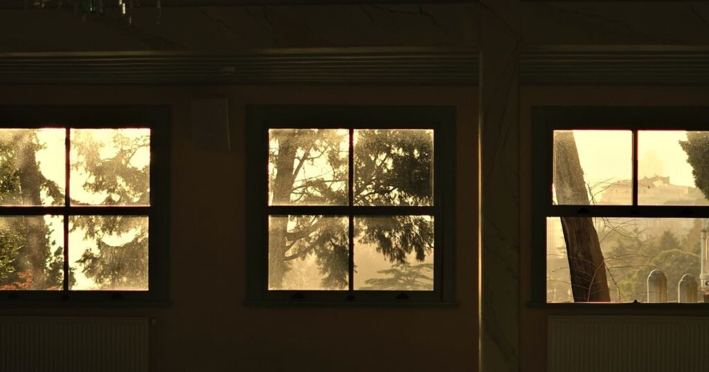 Three tall sash windows filled with warm golden evening light in a dim room