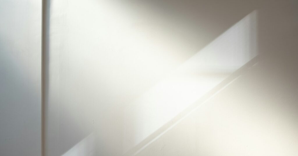 Soft daylight falling across a plain pale wall, with the shadow of a window frame