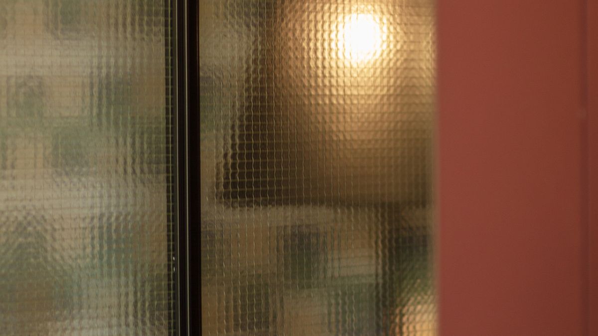 A warm light seen through textured glass beside a terracotta wall, its shape visible but not clear