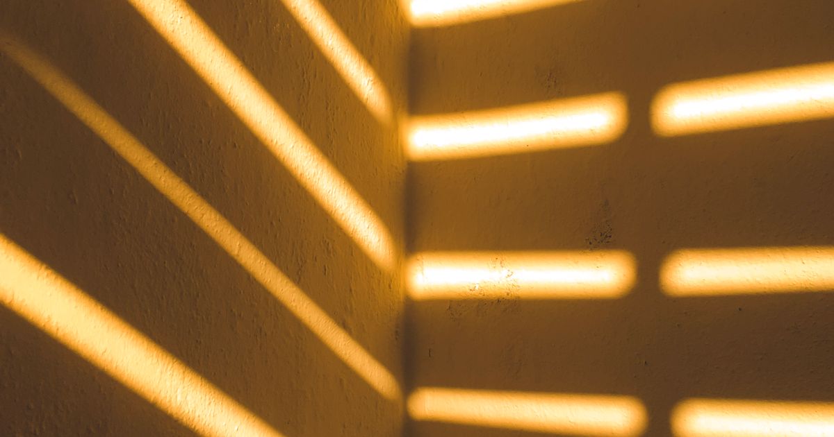 Bands of warm sunlight from a window blind falling across an indoor wall