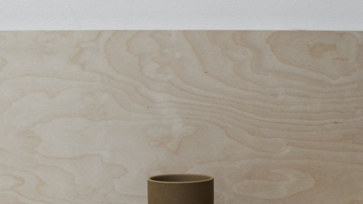 A single small clay cup standing on a pale wooden surface