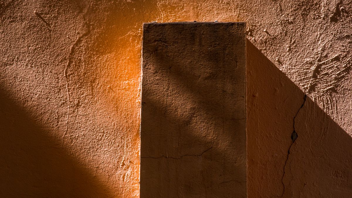 A warm terracotta wall divided by a pillar, one side in light and the other in shadow