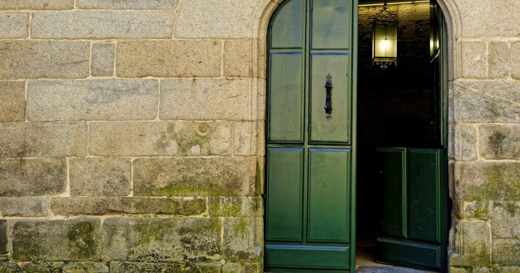 A green door standing ajar in a warm stone wall, with light inside