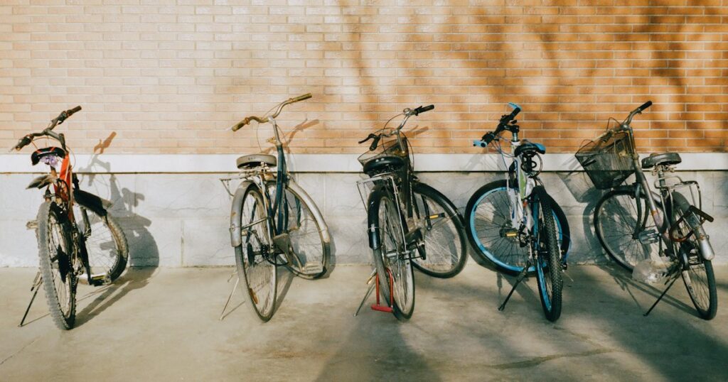 Five bicycles parked side by side against a pale brick wall in warm afternoon light