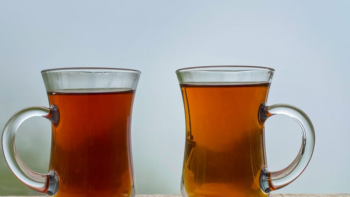 Two amber glasses of tea standing side by side against a pale sky