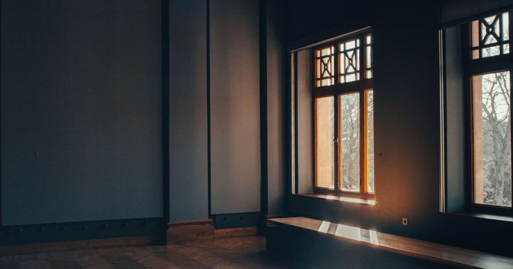 A tall window filled with warm light in an otherwise dim panelled room