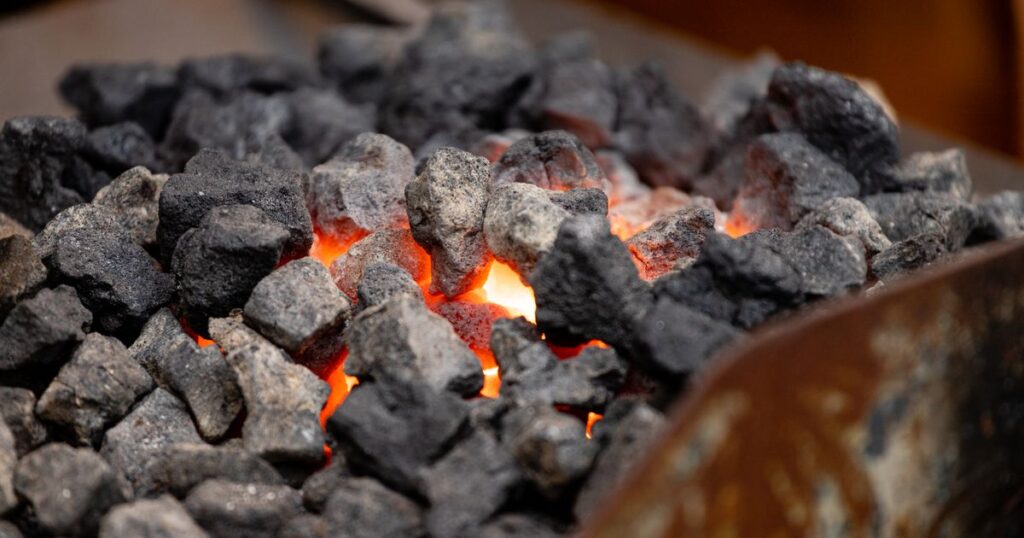 Glowing orange embers showing through a layer of grey ash in a metal fire bowl