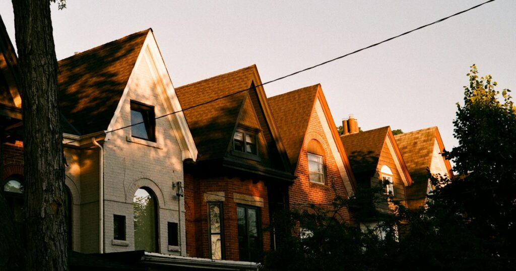 A row of gabled brick and painted houses lit by low golden evening sun, with a bare tree in the foreground