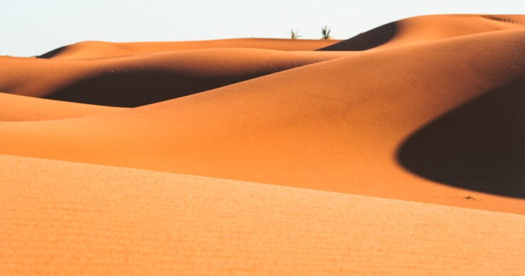 Two sunlit dune ridges running apart with a widening band of shadow between them