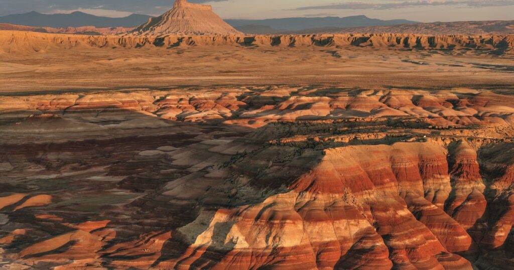 Banded red and ochre desert badlands stretching to a distant butte at sunset