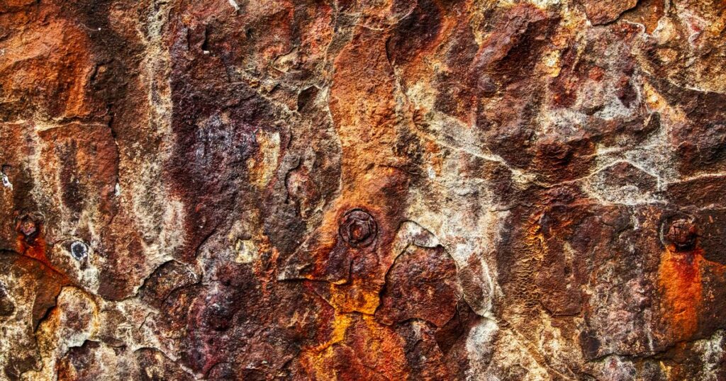 A weathered rock face in rust and ochre, worn into overlapping layers