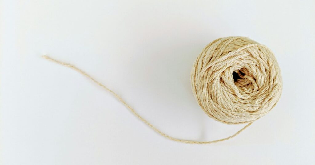 A pale cream ball of string on a white surface with one loose thread trailing away from it