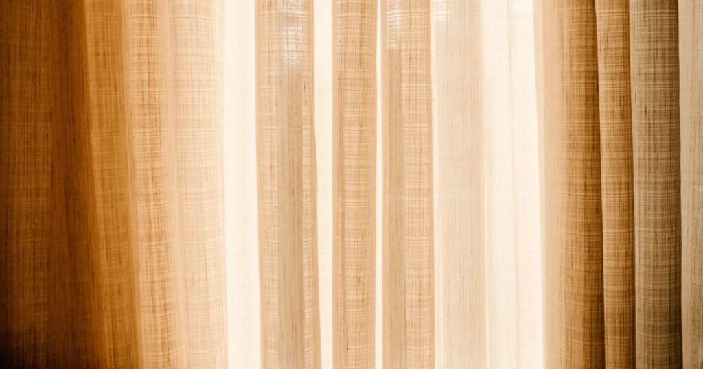 Daylight glowing through a drawn linen curtain in warm cream and brown