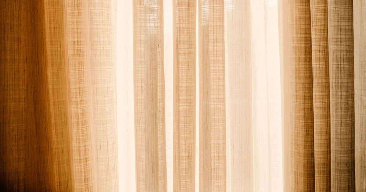 Daylight glowing through a drawn linen curtain in warm cream and brown