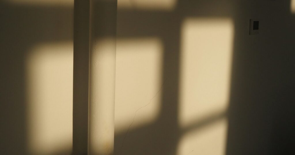 Soft window light falling across a plain warm cream wall in the late afternoon