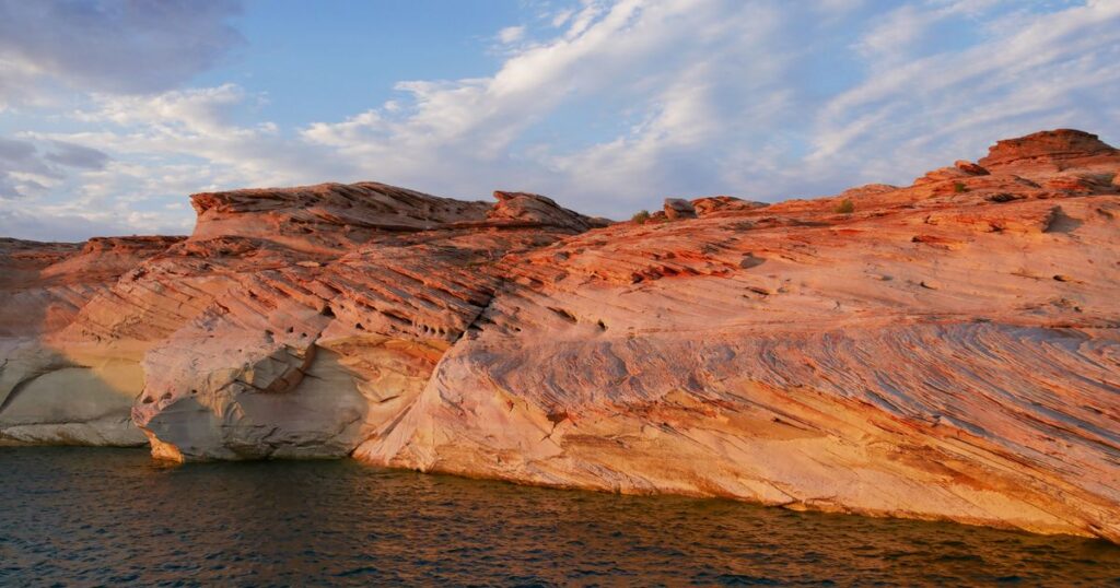 Sandstone cliffs lit apricot and rose by low sunlight above still water