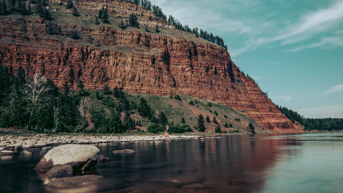 A tall red rock cliff above a river, its whole face repeated in the still water below