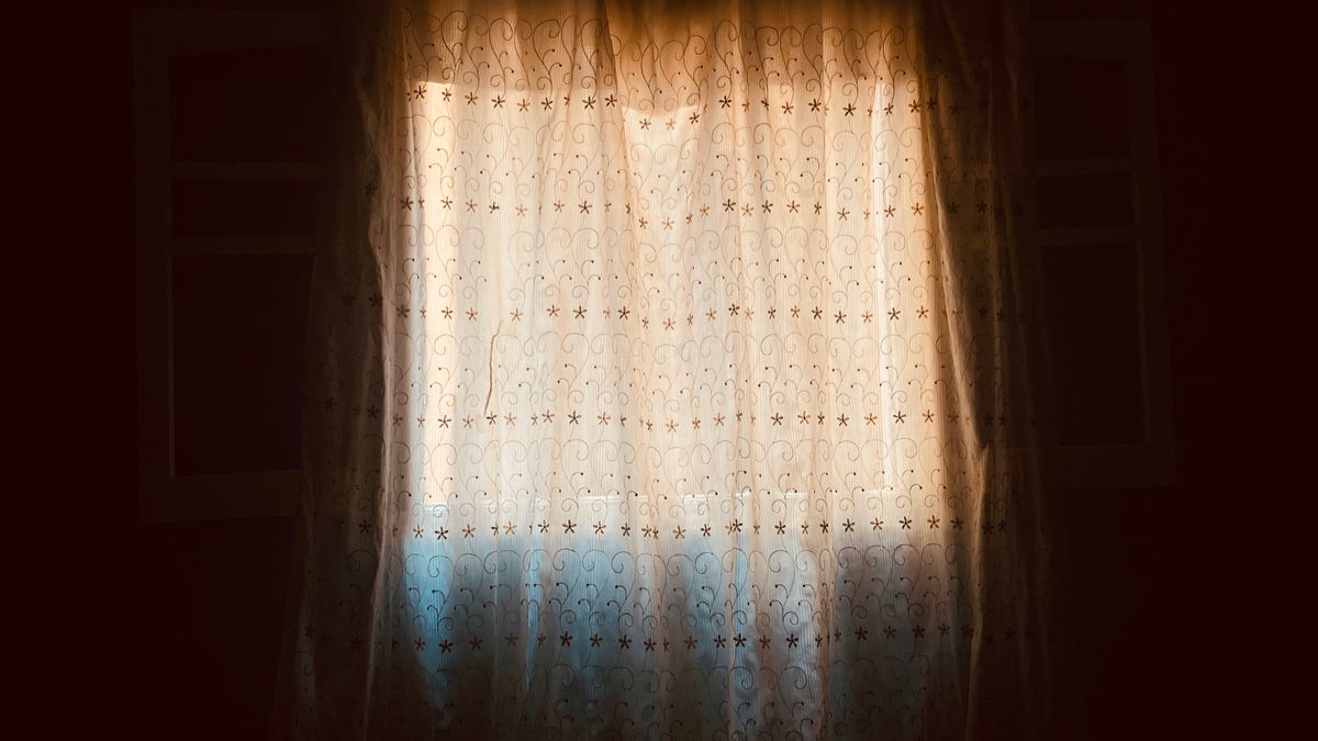 A curtain drawn across a window with morning light behind it