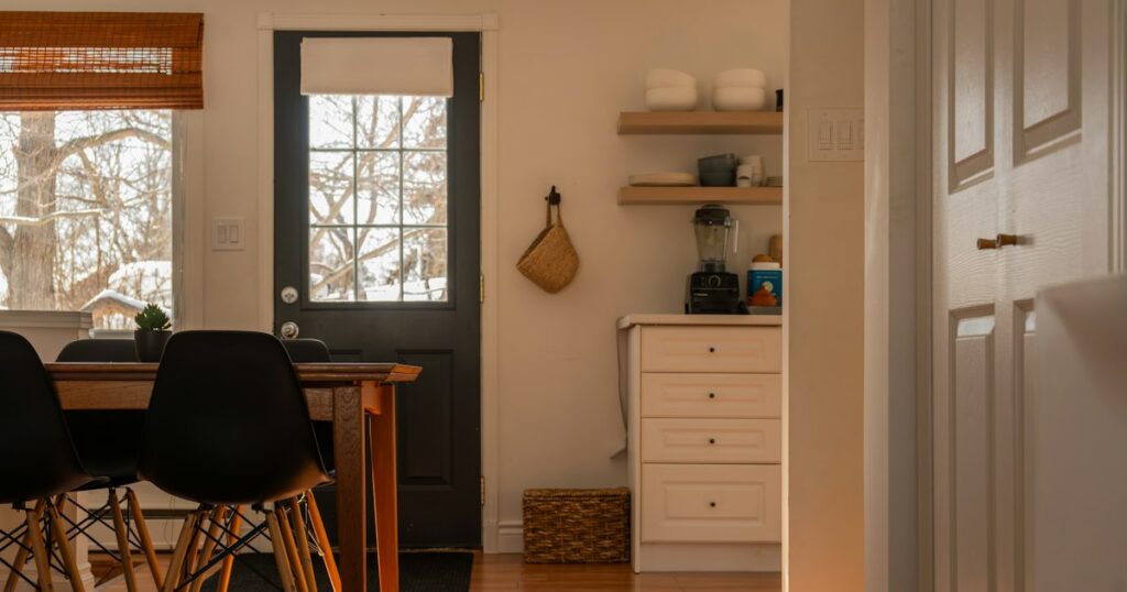 A settled kitchen and dining corner with a wooden table, chairs and daylight through the back door