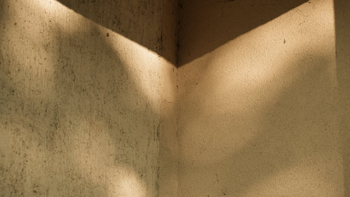 Sunlight and shadow moving across the warm plaster walls of an empty corner