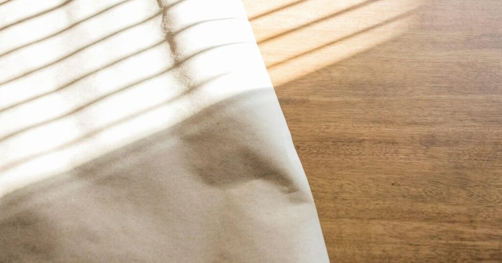 Folded pale linen cloth on a wooden table, crossed by warm stripes of window light