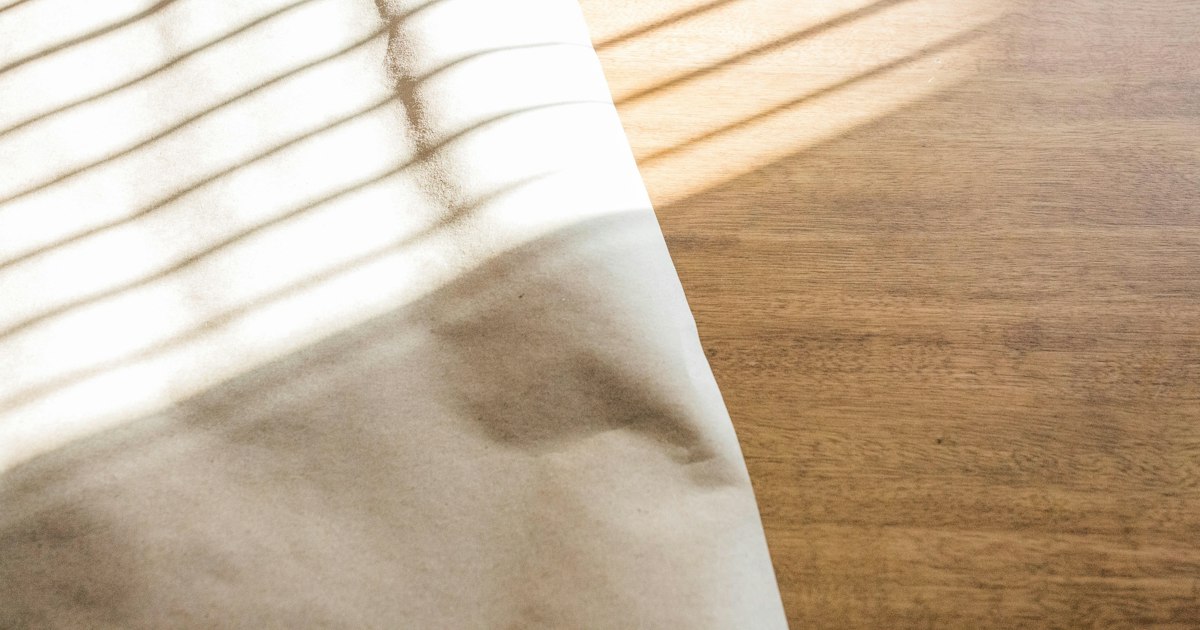 Folded pale linen cloth on a wooden table, crossed by warm stripes of window light
