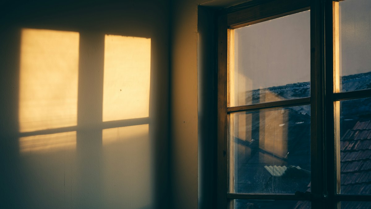 Low evening sun coming through an old window and falling on a plain wall.