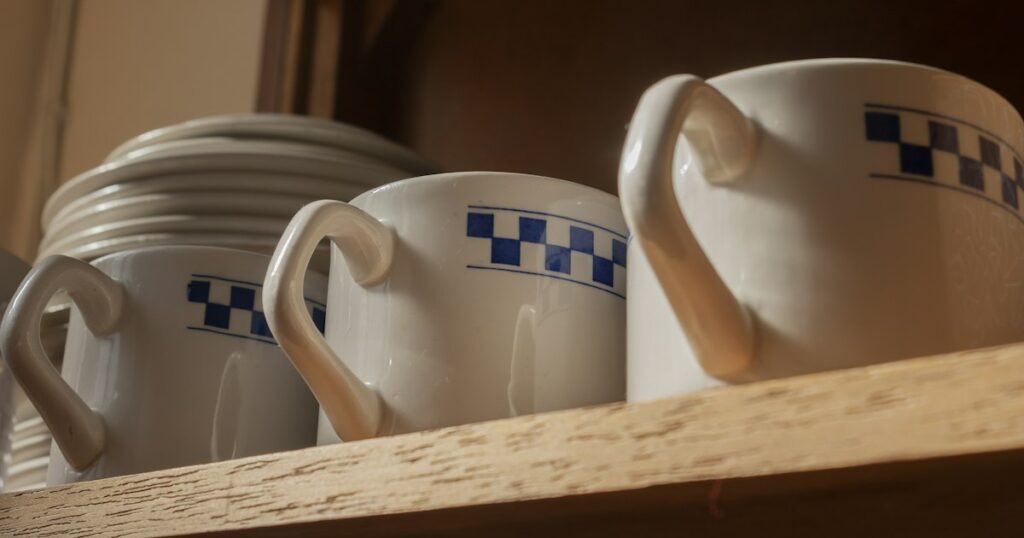 Three matching blue and white cups standing in a row on a wooden shelf