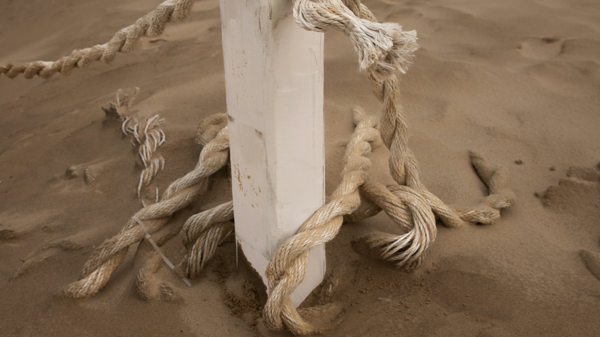 A rope boundary tied to a white post in drifting sand