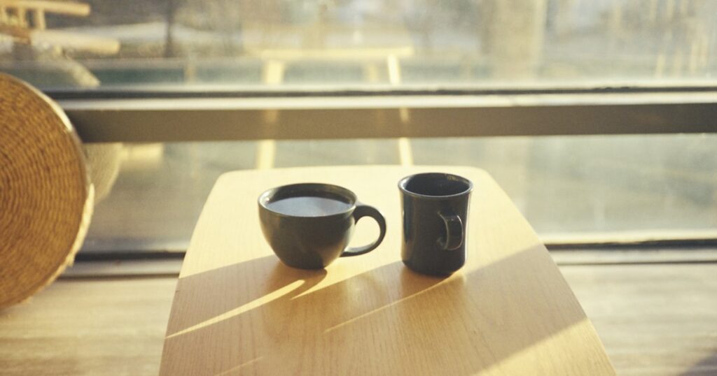 Two cups on a small wooden table in low sunlight by a window