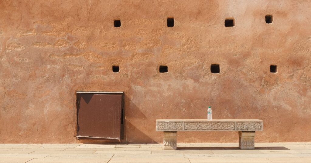 A carved stone bench standing alone against a warm terracotta wall beside a closed door