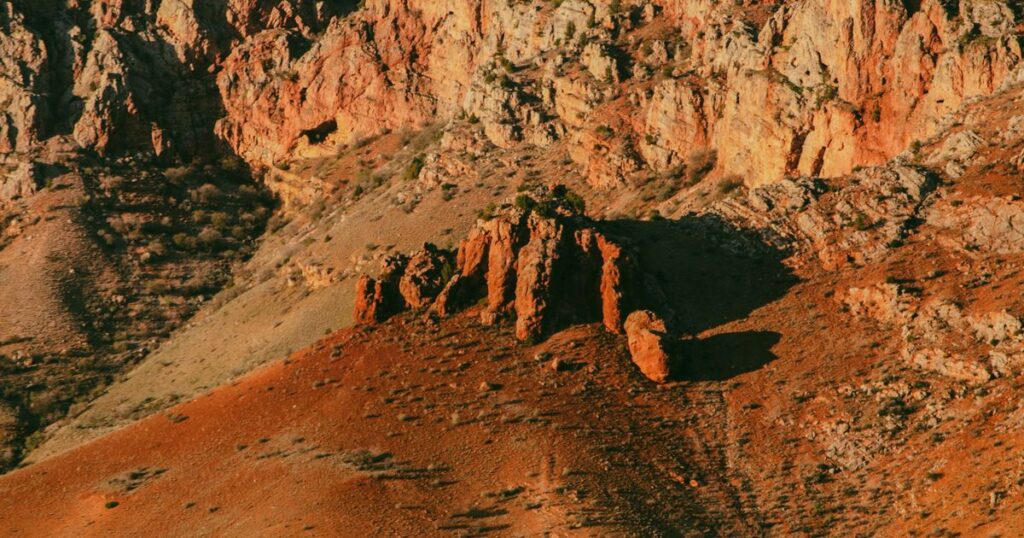 A red rock hillside in low sunlight, one slope lit and the other in shadow