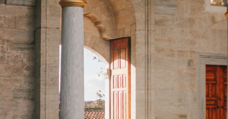 Sunlight falling through a stone archway onto a tall open wooden door