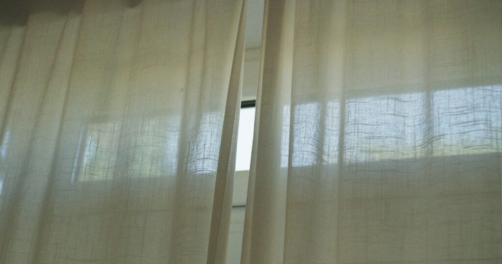 Sheer pale curtains drawn across a window with daylight behind them