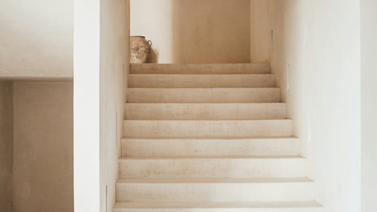Pale plaster stairs rising to a landing that turns out of sight, with a clay jar at the top
