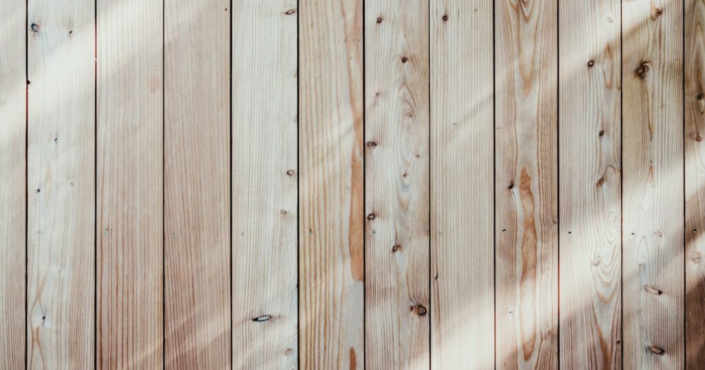 Pale weathered wooden boards running side by side, crossed by a band of soft daylight