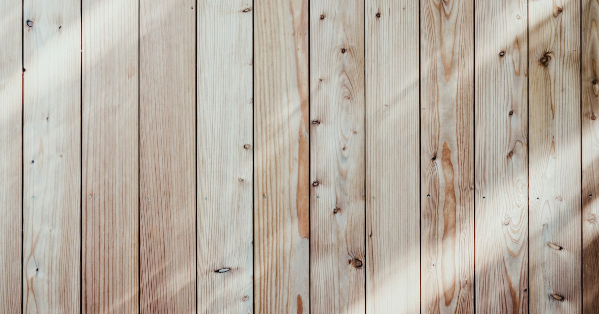 Pale weathered wooden boards running side by side, crossed by a band of soft daylight